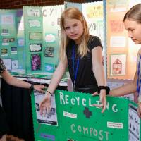 Three students hold up a recycling and compost sign